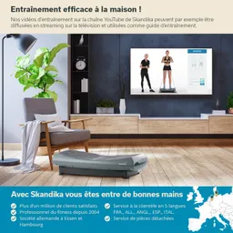 Wohnzimmer mit einem grauen Fitnessgerät im Vordergrund. Auf einem Fernseher wird eine Trainingsanleitung angezeigt. Pflanzen und Möbel sichtbar.