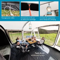 Zeltinnenansicht mit vier Personen, die an einem Tisch sitzen. Hängende Lampe und Schlafbereich sichtbar.
