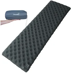 Schlafmatte in dunklem Grau mit gepolstertem Design. Links ist eine zusammengepackte Version in einer Hand sichtbar.