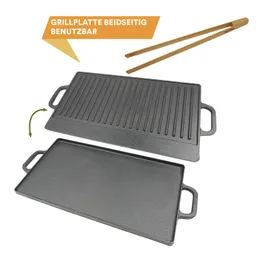 Grillplatte aus Gusseisen, beidseitig nutzbar, mit einer griffigen Seite und einer flachen Seite. Zwei Griffe an den Seiten. Holz-Zangen daneben.