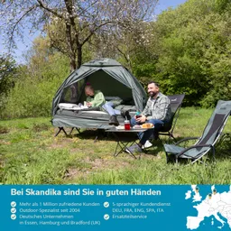 Zelt in der Natur mit einer Person im Zelt und einer weiteren Person, die an einem Tisch sitzt. Umgeben von Bäumen und Gras.