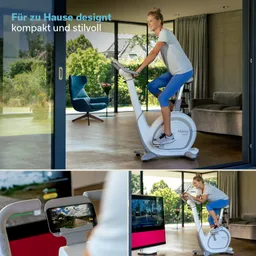 Eine Person fährt auf einem Fitness-Bike in einem modernen Raum mit großen Fenstern. Im Hintergrund ist ein Sitzbereich und ein Garten sichtbar. Ein Bildschirm zeigt eine Trainingsanzeige.