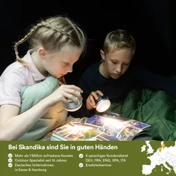 Zwei Kinder betrachten ein Fotobuch im Dunkeln, beleuchtet von Taschenlampen. Sie sitzen in einem Zelt.