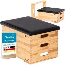 Holzbox mit schwarzem Sitzpolster, seitlich zwei Grifflöcher, im Vordergrund ein Etikett.