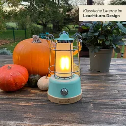 Klassische Laterne im Leuchtturm-Design mit orangefarbenem Kürbis und weiteren Dekorationsgegenständen auf einem Holztisch.