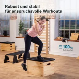 Person steht auf einer stabilen Holzbox und bereitet sich auf einen Sprung vor. Im Hintergrund sind weitere Fitnessgeräte sichtbar.