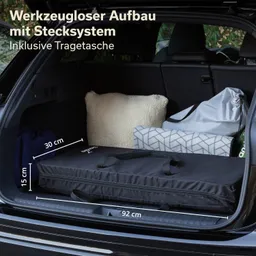 Kofferraum eines Autos mit einer schwarzen Tasche, einem Kissen, einer Decke und einer Tragetasche. Maße sind eingezeichnet.