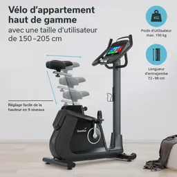 Fitnessbike mit verstellbarem Sitz und Bedienfeld. Maximales Benutzergewicht 150 kg. Raum mit Holzfußboden und Bettdecke.