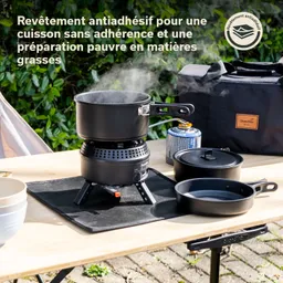 Ein mobiler Gaskocher mit einem schwarzen Topf und zwei weiteren schwarzen Kochgeräten auf einem Tisch. Dampfformation aus dem Topf.