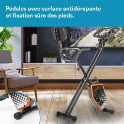 Fahrradergometer mit rutschfesten Pedalen in einem modernen Raum mit Pflanzen und einem Holzschrank im Hintergrund.