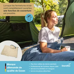 Person liegt in einem Schlafsack im Freien, umgeben von Bäumen und Zelten. Eine Tasse ist in ihrer Hand.