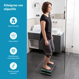 Eine Person steht barfuß auf einer digitalen Waage in einem Badezimmer. Im Hintergrund sind Handtücher und ein Waschbecken sichtbar.