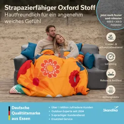 Eine Person und eine Person sitzen auf einer Couch im Freien, eingekuschelt in eine bunte Decke mit floralen Mustern.