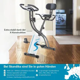 Fahrrad-Ergometer mit X-Konstruktion, montiert auf einem Holzfußboden in einem Raum mit einem Türöffnungsbereich im Hintergrund.