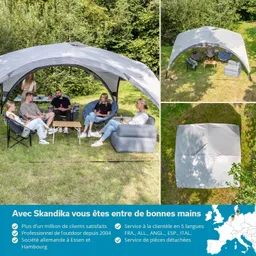 Sechs Personen sitzen unter einem großen grauen Pavillon auf einer grünen Wiese. Um sie herum sind Sitzgelegenheiten und ein Tisch. Im Vordergrund steht ein Holztablett mit Getränken. Im Hintergrund ist dichter Baumwald sichtbar.