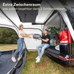 Zwei Personen stehen an einem Fahrzeug, während eine Person eine Tasche übergibt. Im Hintergrund ist ein Zelt erkennbar.