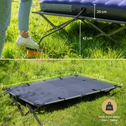 Faltbare Campingliege auf grünem Gras mit Maßen und einem Fuß, der auf eine Pumpe zeigt. Die Liege ist schwarz und kompakt.