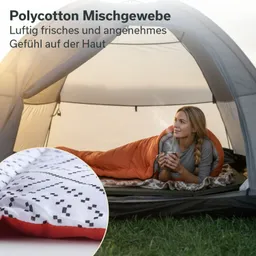 Campingschlafsack in orange und grauem Muster, eine Person liegt darin und hält eine Tasse, im Zelt auf Gras.