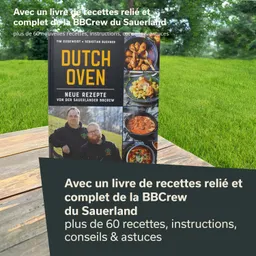 Ein Kochbuch mit dem Titel "Dutch Oven" steht auf einem Tisch. Im Hintergrund ist eine grüne Wiese sichtbar. Das Buch enthält Bilder von Gerichten und Informationen zu Rezepten.