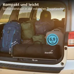 Im Kofferraum eines Fahrzeugs sind mehrere Taschen und Rucksäcke unterschiedlicher Farben gestapelt. Eine schwarze Tragetasche mit Logo ist im Vordergrund sichtbar, daneben eine laufende Maßangabe.