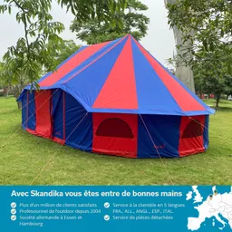 Buntes Zelt mit einem blau-rot gestreiften Dach, umgeben von Bäumen auf einer Wiese.