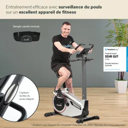 Mann sitzt auf einem Fitnessgerät und nutzt es. Das Gerät hat ein Display und integrierte Pulssensoren. Hintergrund ist grau.