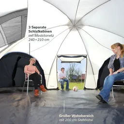 Großes Zelt mit drei Schlafkabinen, innen sitzen drei Personen, darunter ein Fußball, kahle Bäume im Hintergrund.