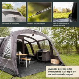 Campingtent mit einem offenen Bereich, einem Tisch, einer Kochstelle und robusten Bodenmatten. Im Hintergrund Bäume und Wiese.