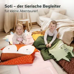 Zwei Kinder sitzen auf bunten, tierförmigen Kissen und Decken. Im Hintergrund steht ein Tisch und ein Bett.