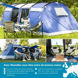 Ein großes, blaues Zelt steht auf einer Wiese, umgeben von Campingstühlen und einem Tisch. Im Hintergrund Bäume.