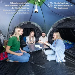 Vier Personen sitzen in einem Zelt um einen Tisch und spielen Karten. Das Zelt hat eine silberne Außenbeschichtung.