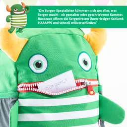 Grüner Rucksack in Form eines Monsters mit großen Augen und Hörnern. Eine Notiz mit dem Wort „Sorgen“ steckt in einem Reißverschlussfach.