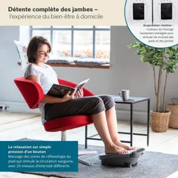 Eine Person sitzt in einem roten Stuhl, liest ein Buch und hat Füße auf einem Massagergerät. Neben ihr steht ein Tisch mit einer Tasse.