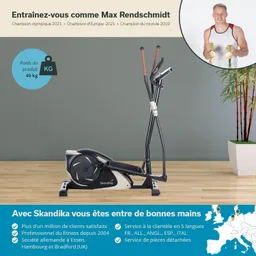 Es handelt sich um ein Fitnessgerät, einen Crosstrainer, auf einem Holzfußboden. Im Hintergrund sind eine grüne Wand und eine Pflanze zu sehen. Oben rechts ist ein Porträt einer Person sichtbar, die Medaillen hält.