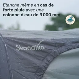 Zeltmaterial mit Wasserperlen, das Logo „Skandika“ in grau, Hintergrund unscharf mit grünem Umfeld.
