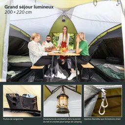 Innenansicht eines Zeltes mit vier Personen an einem Tisch, umgeben von Campingausstattung. Es gibt eine Hängeleuchte und Stauraum-Taschen.