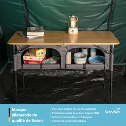 Ein klappbarer Tisch aus Holz mit einer Lampe, Spielen und Geschirr in einem Zelt. Grün gewebte Zeltwände im Hintergrund.