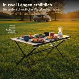 Ein Tisch auf einer Wiese mit verschiedenen Speisen und Getränken. Im Hintergrund ein Fahrzeug und Sonnenuntergang.