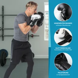 Mann in Sportbekleidung trägt schwarze Boxhandschuhe, steht in einem Fitnessstudio mit Gewichten im Hintergrund.