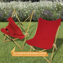 Zwei rot-bezogene Klappstühle aus Holz stehen auf grünem Gras, im Hintergrund blühende Pflanzen.