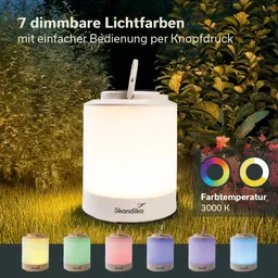 Tischlampe in Weiß mit einer glatten, runden Form. Sechs weitere kleine Lampen in verschiedenen Farben darunter. Hintergrund mit grünen Pflanzen.