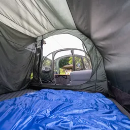 Zeltinnere mit blauem Schlafsack auf dem Boden. Sicht auf den Zeltausgang und eine sitzgelegenheit im Hintergrund.