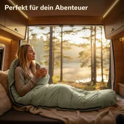 Eine Person sitzt in einem Schlafsack auf einer Couch in einem Fahrzeug. Sie hält eine Tasse, während sanftes Licht durch ein Fenster strömt, das auf einen Waldblick fällt.