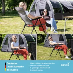 Zwei Personen sitzen in Gartenstühlen auf einer Wiese vor einem Zelt. Die Umgebung ist grün mit Bäumen und Gras.