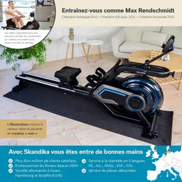 Rudergerät auf einem schwarzen Teppich in einem modernen Raum mit einer Pflanze und einem hellen Sofa im Hintergrund.