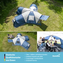 Großes, mehrteiliges Zelt in blau und grau auf einer Wiese, umgeben von Bäumen. Gruppen von Personen sitzen am Tisch und essen.