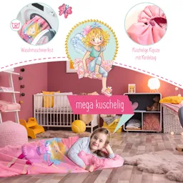 Liegendes Kind auf einer Decke mit einem bunten Design, umgeben von Möbeln in einem Kinderzimmer. Hintergrund in Rosa.