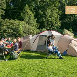 Zelt in der Natur mit mehreren Personen am Tisch, eine sitzende Person liest. Grüne Wiese, Bäume im Hintergrund.