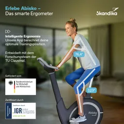 Ergometer mit einer Person, die in Trainingsposition sitzt. Helle Umgebung mit grünen Pflanzen im Hintergrund.