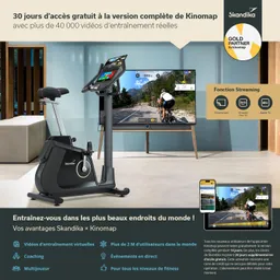 Ein Stationäres Fahrrad steht vor einem Fernseher, auf dem ein Radfahrer in einer Landschaft zu sehen ist. Informationen zu einem Fitnessprogramm sind sichtbar.